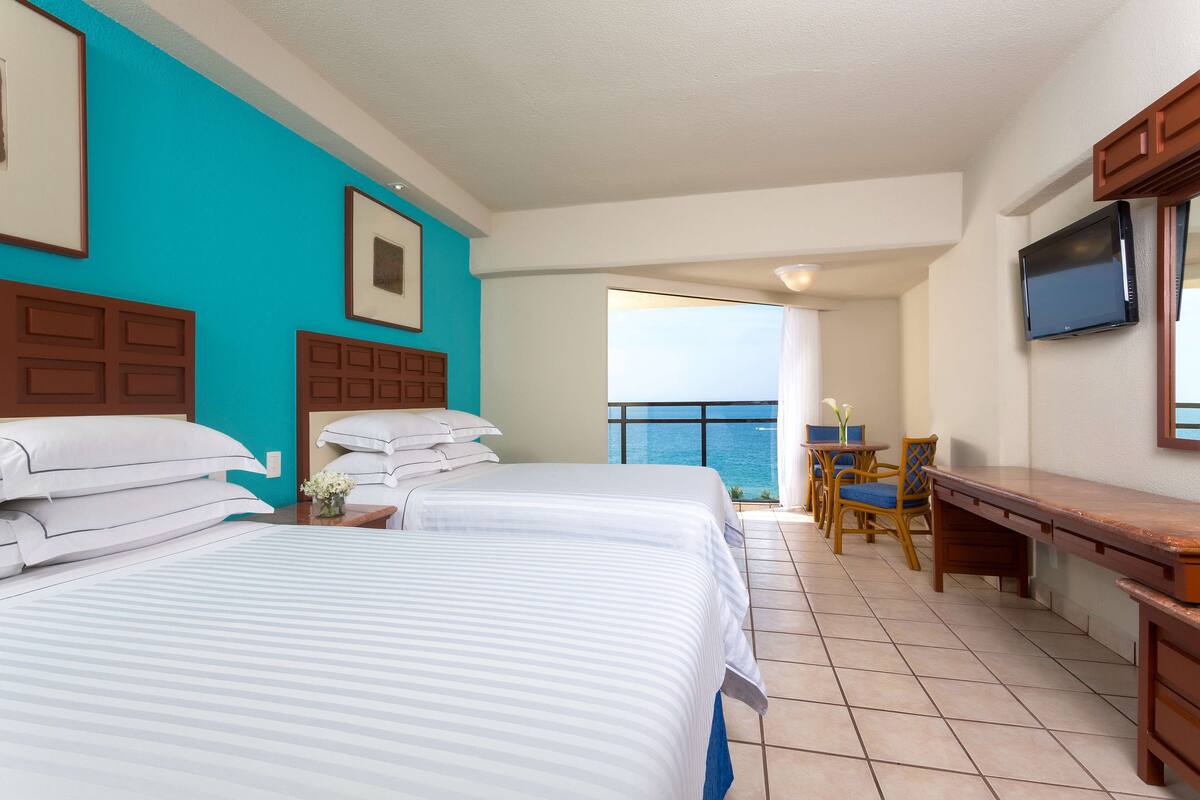A hotel room with two beds, a balcony with a view, a desk, and a TV.