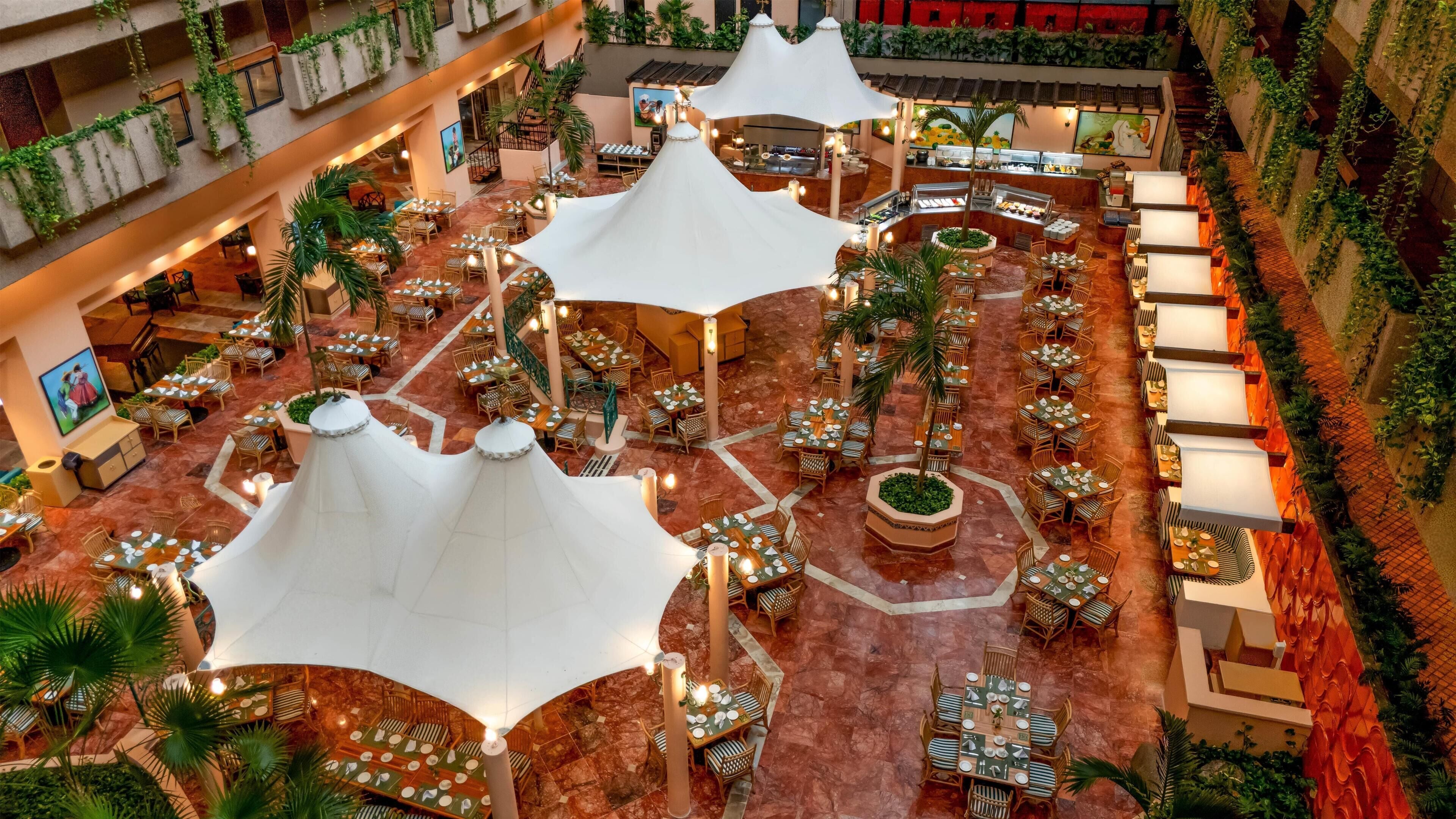 Un espace de restauration intérieur à plusieurs niveaux, doté de tables et de chaises, et agrémenté de plantes et d’un éclairage décoratif.