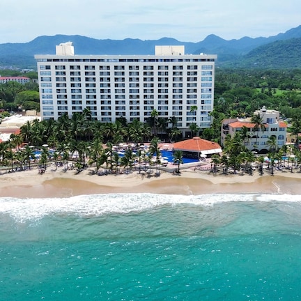 A beachfront hotel with multiple buildings, a pool area, and a beach with palm trees.