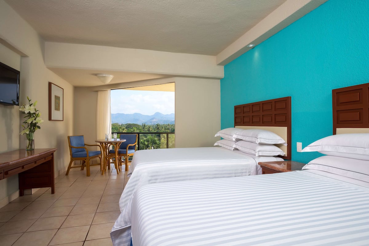A hotel room with two beds, a desk, a chair, and a view of mountains.