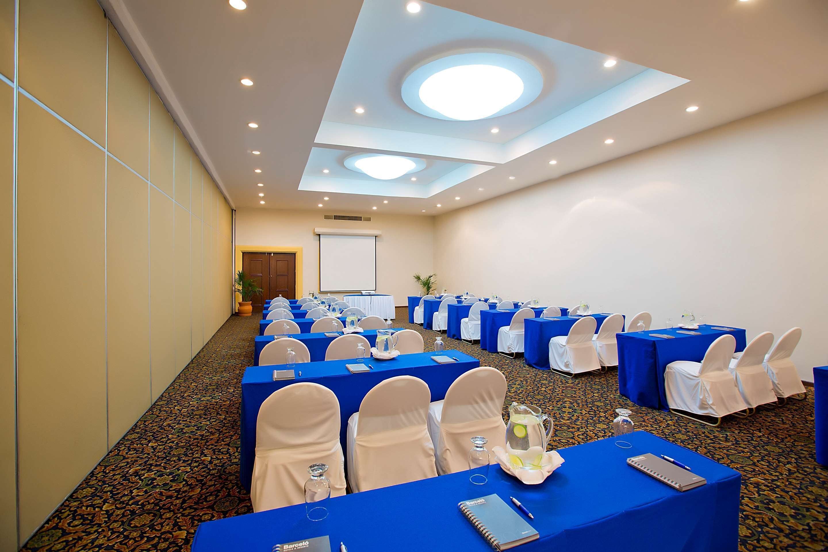 Sala de conferências com mesas, cadeiras e uma tela de projeção.