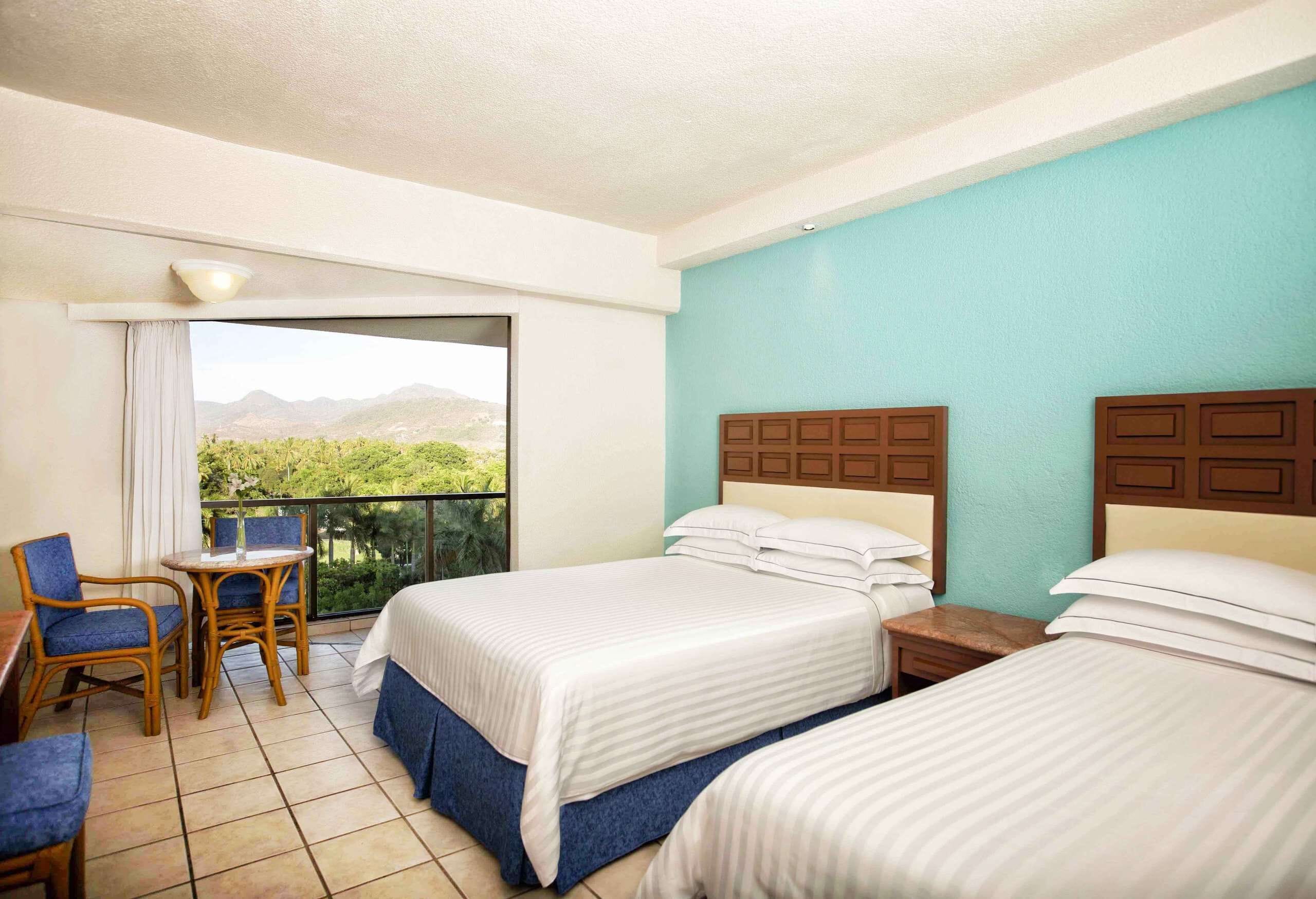A hotel room with two beds, a balcony with a view, a small table, and a chair.