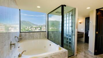 Une salle de bain dotée d’une grande baignoire, d’une douche à parois de verre et offrant une vue sur le paysage urbain.