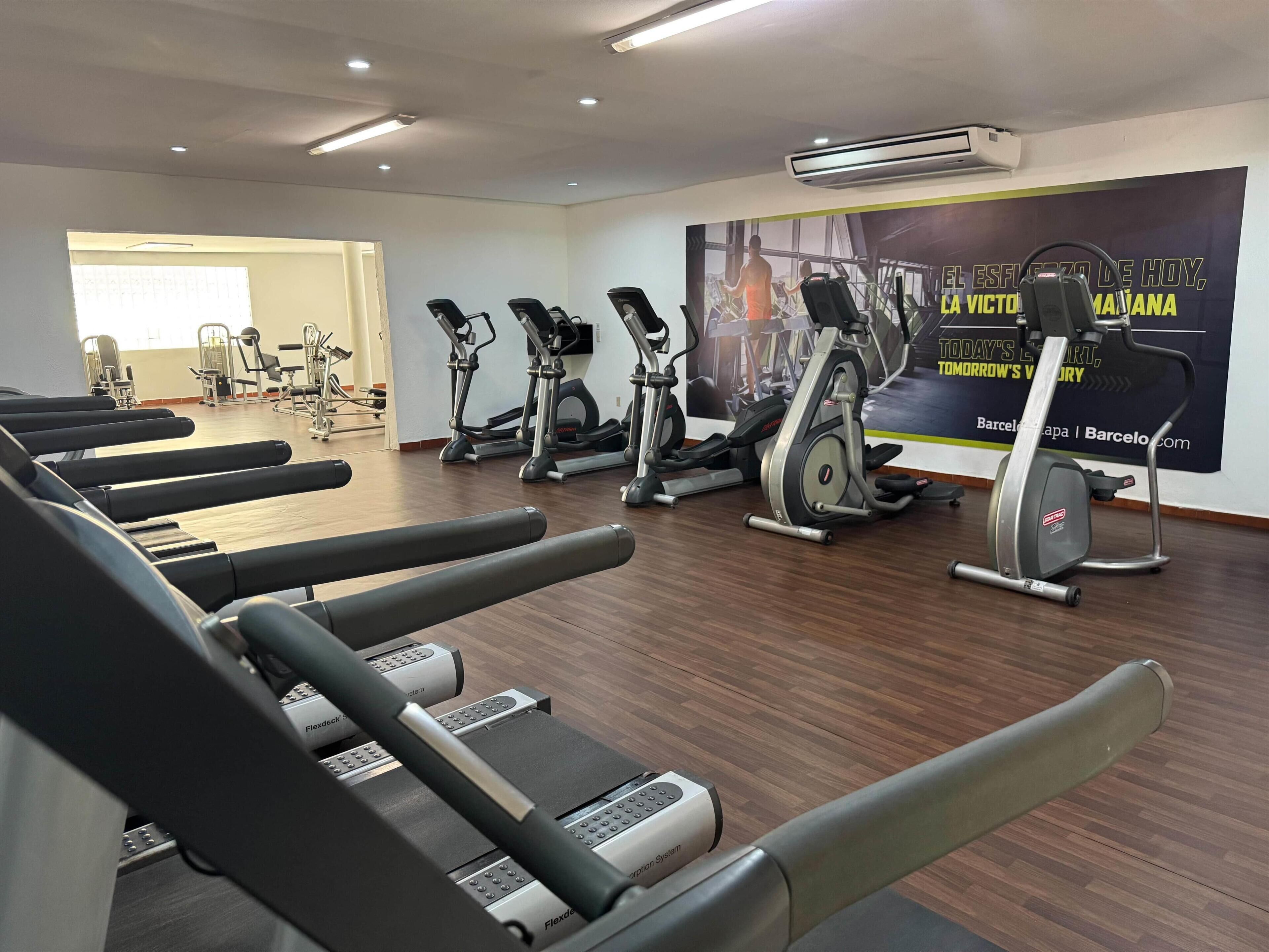 A gym with multiple treadmills, stationary bikes, and a wall with motivational text.