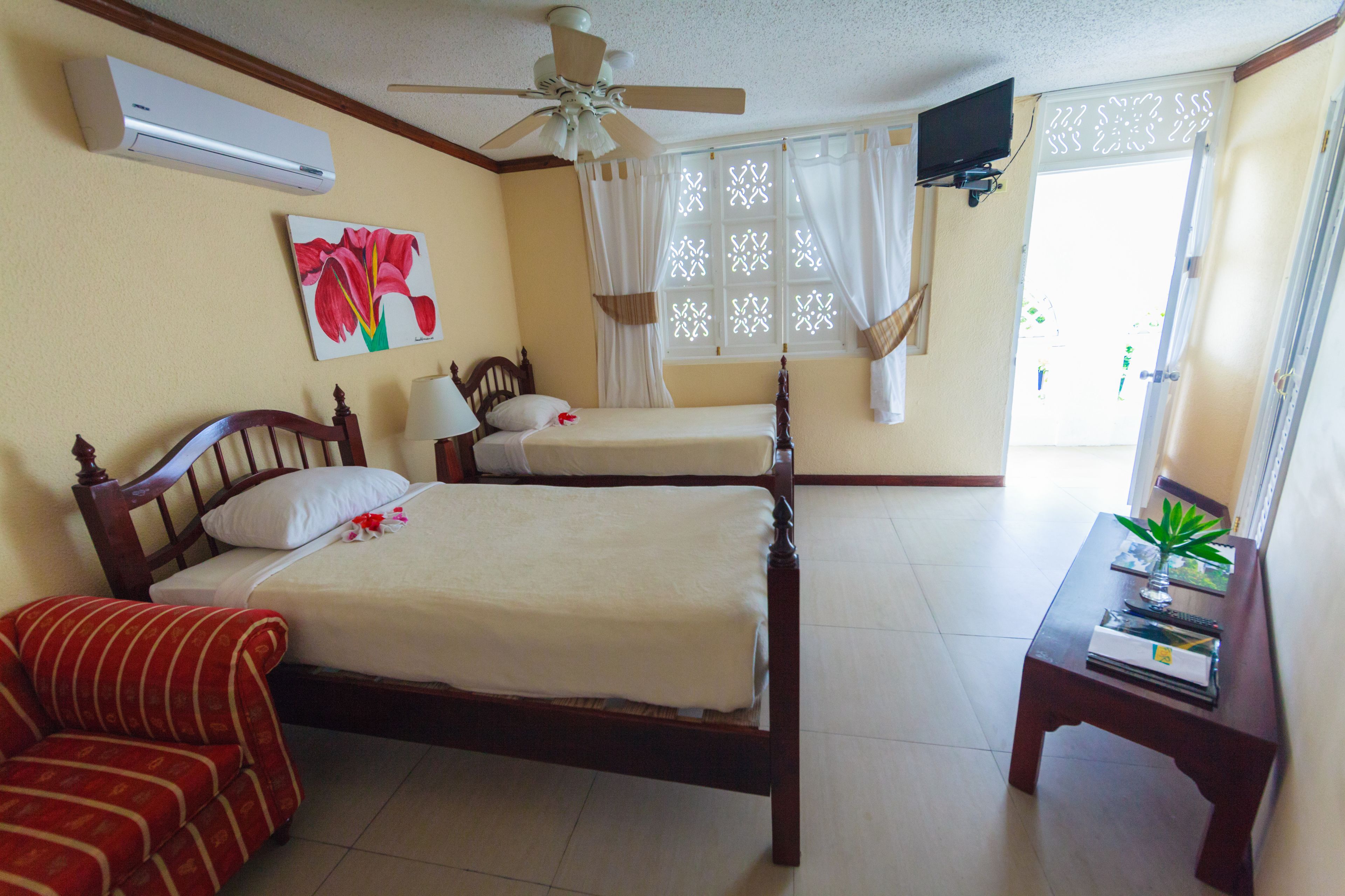 Habitación de hotel con dos camas, ventilador de techo, aire acondicionado, televisión y ventana con cortinas.