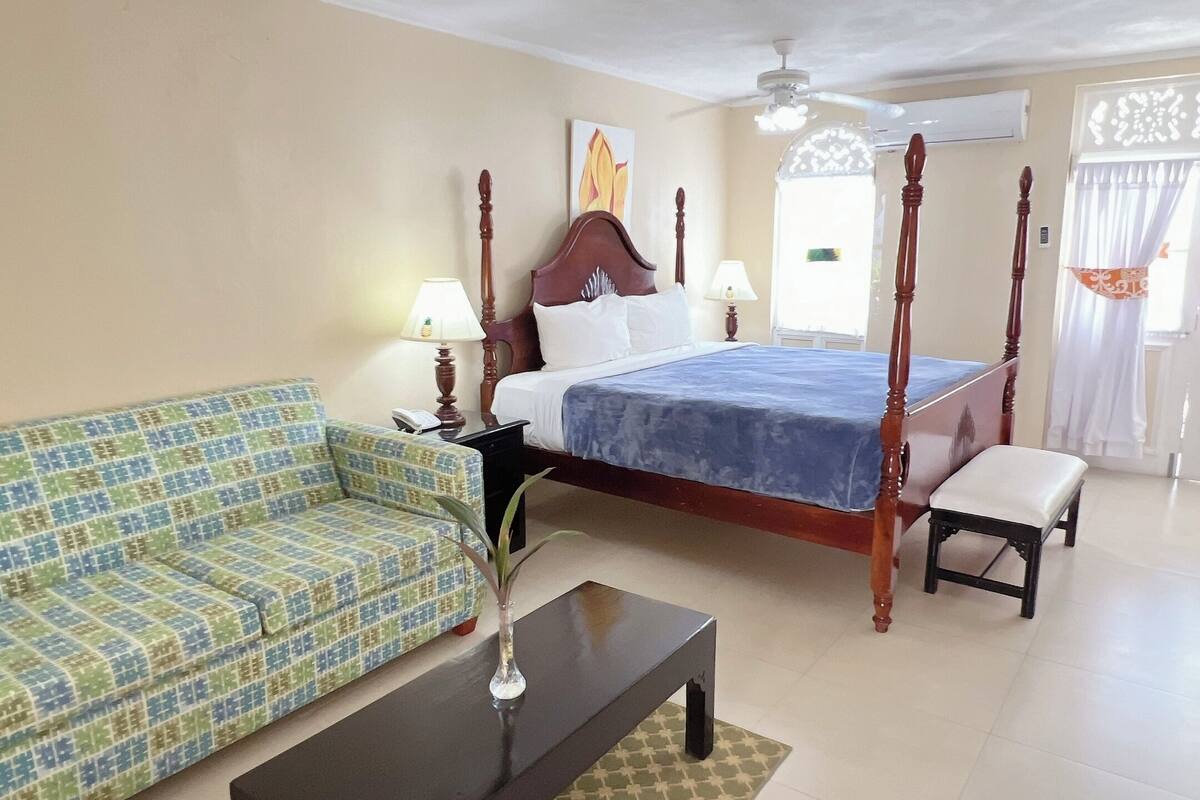 Habitación de hotel con cama con dosel, un sofá, una mesita y una ventana con cortinas.