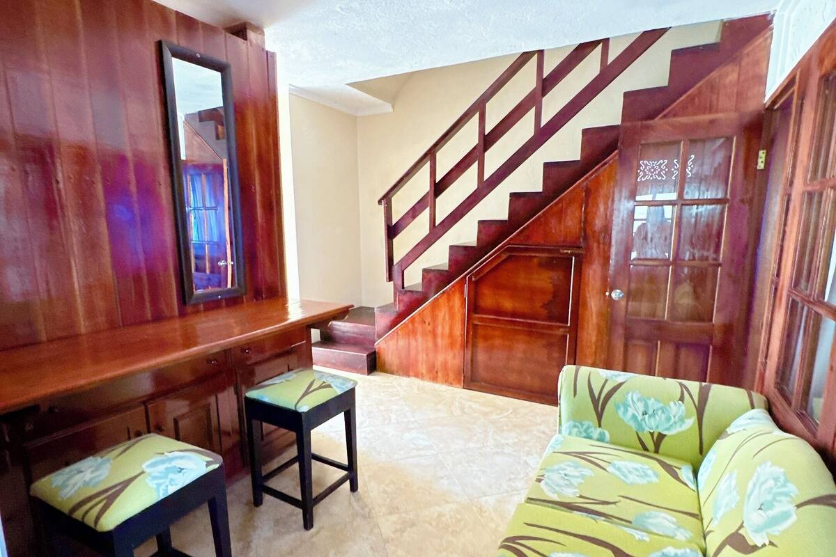Una sala de estar con una escalera de madera, un sofá con tapicería floral y una mesa de centro de madera.