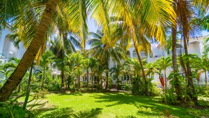 A lush garden with palm trees and a white building with blue accents. - Franklyn D. Resort & Spa (Runaway Bay)