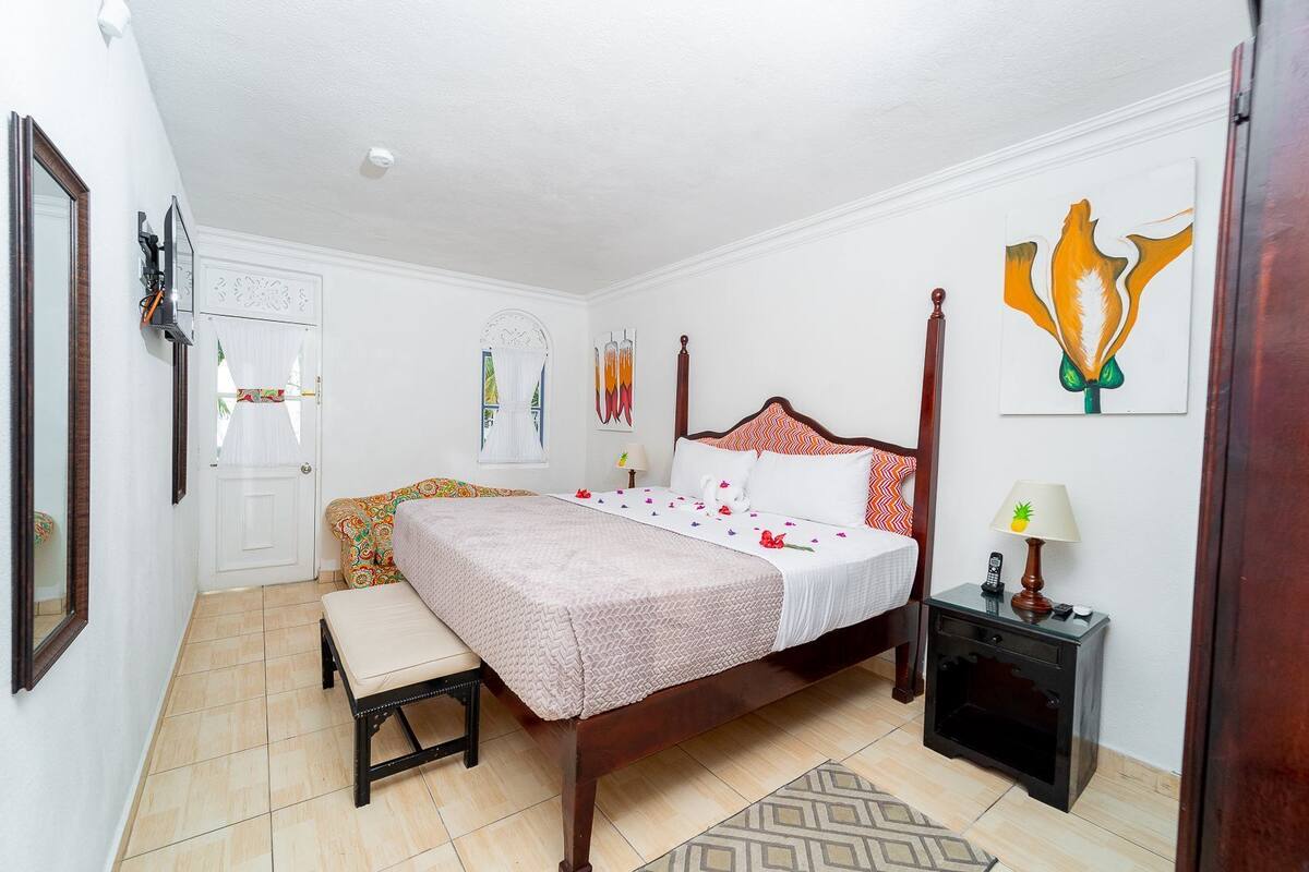 Un dormitorio con una cama con dosel, una mesita de noche con lámpara, una pequeña silla y otro mueble auxiliar.
