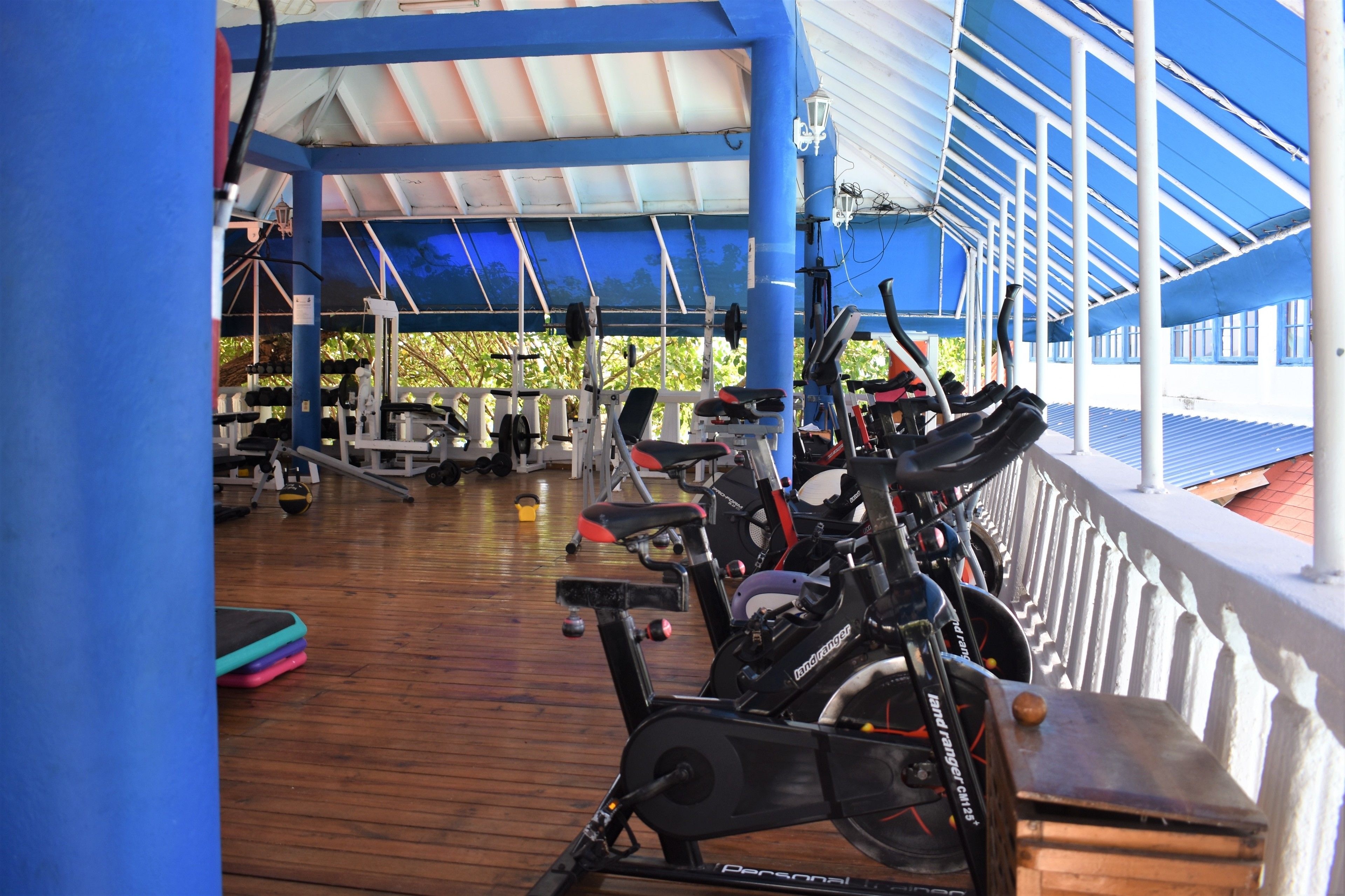 A covered gym area with exercise equipment, including stationary bikes and weight machines.