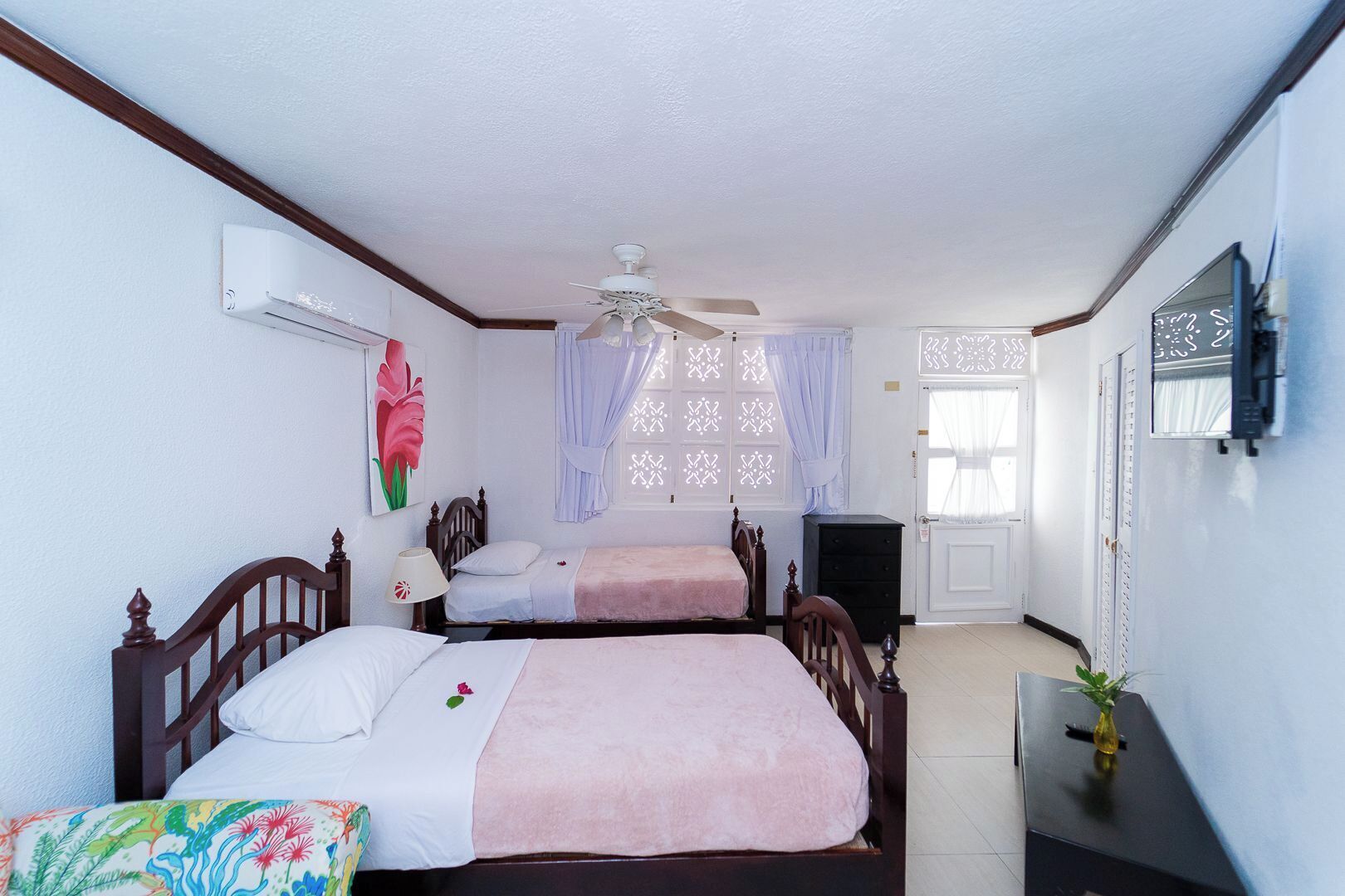 A bedroom with two beds, a ceiling fan, a TV, and a window with decorative shutters.