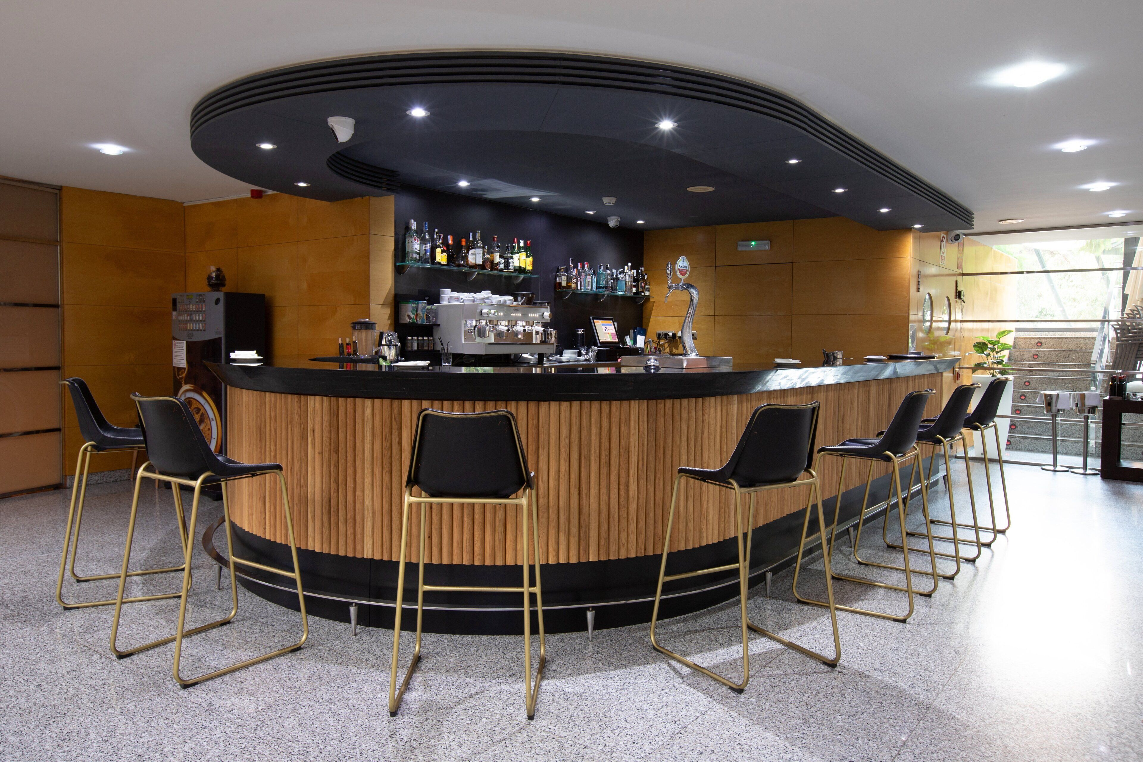 Un área de bar moderna con una barra curva, taburetes y una estantería bien surtida con varias botellas.