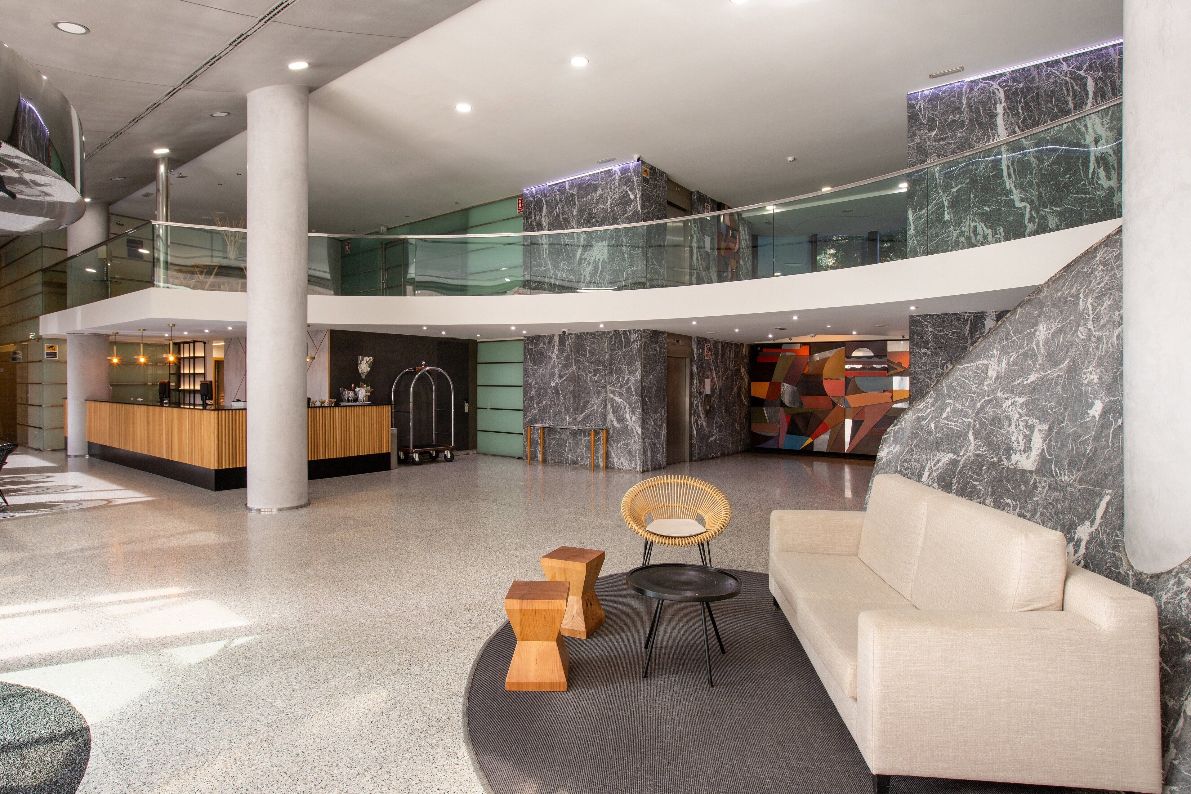 Un hall d’entrée spacieux avec un plafond haut, des murs en marbre et un espace de détente central comprenant un canapé et des tabourets en bois.