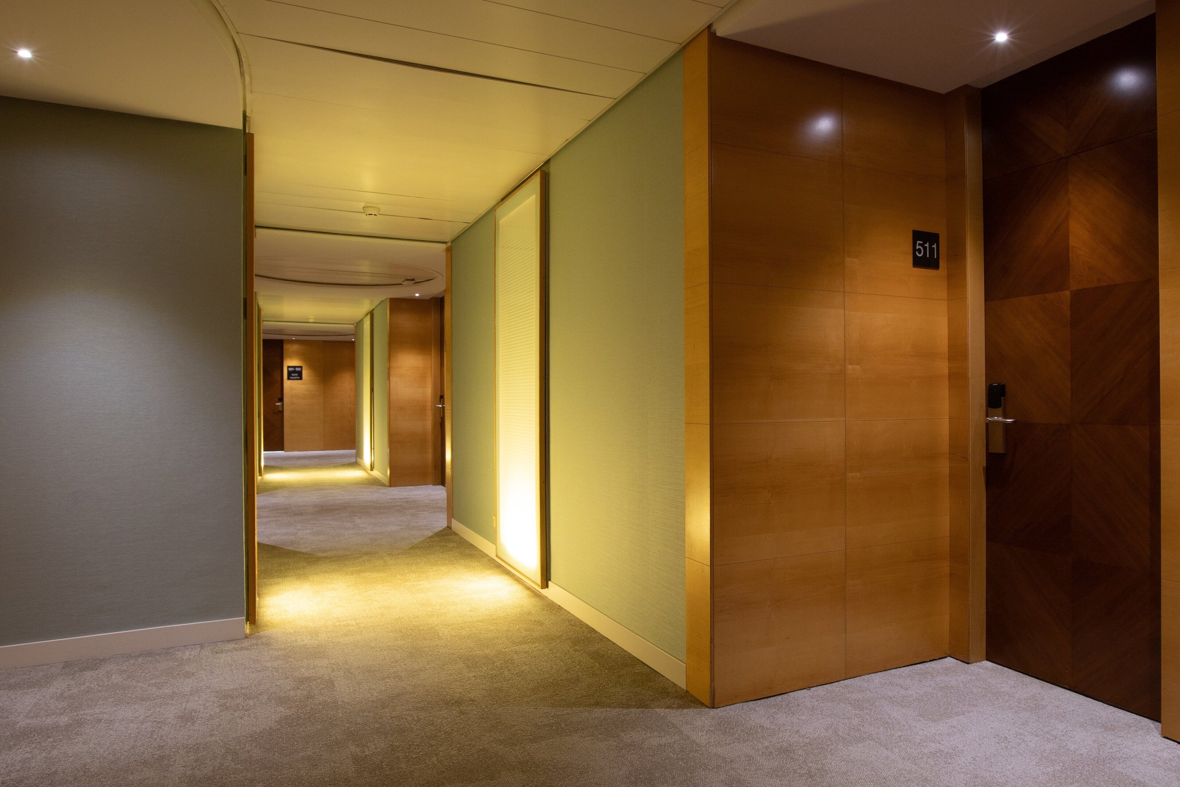 Un pasillo moderno de hotel con piso alfombrado, paredes de madera y una puerta con el número 511.
