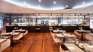 A modern restaurant with a central counter displaying food items, surrounded by tables and chairs. - Hotel Eurostars Acteón (Valencia)