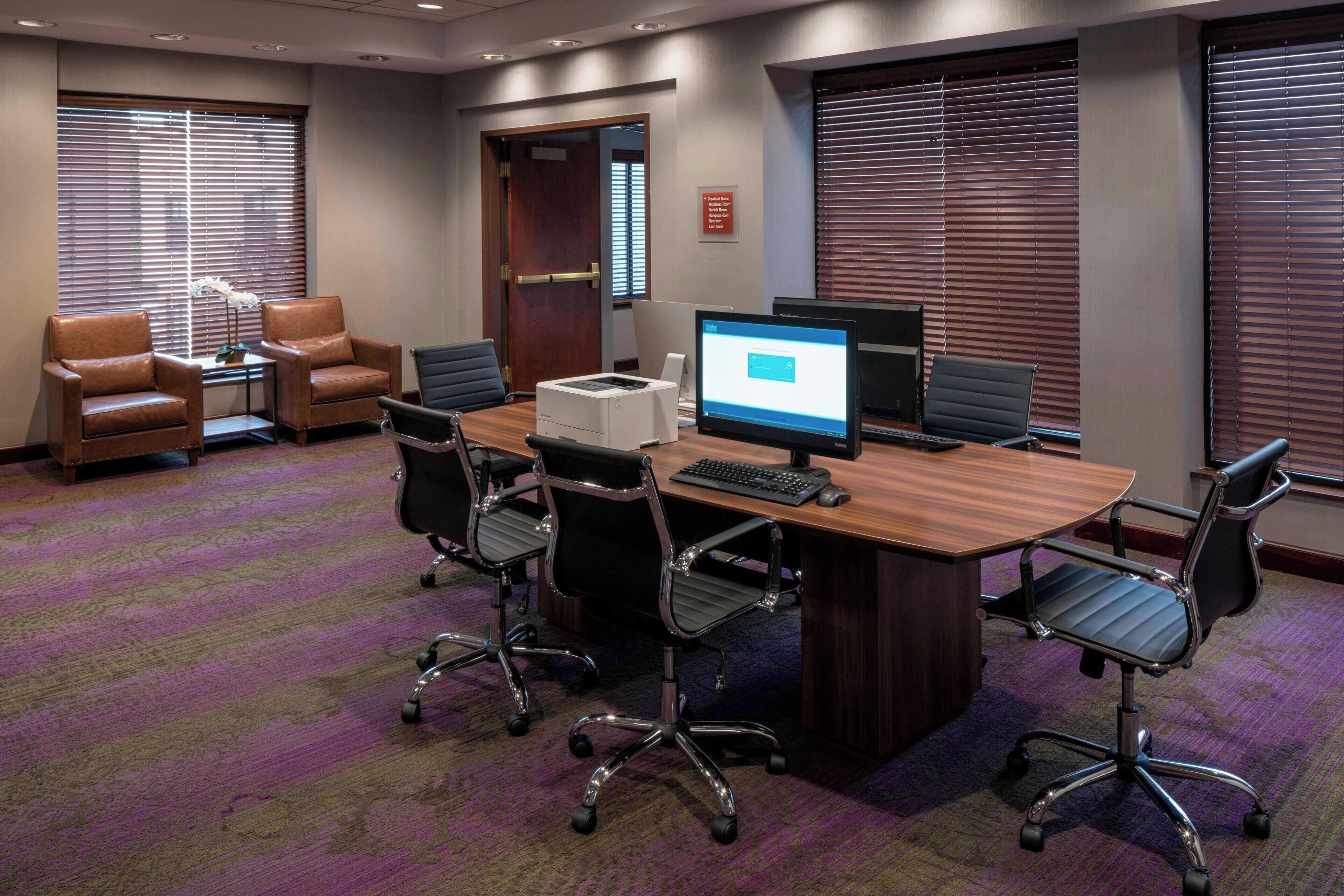 A conference room with a wooden table, four office chairs, a computer, and a printer.
