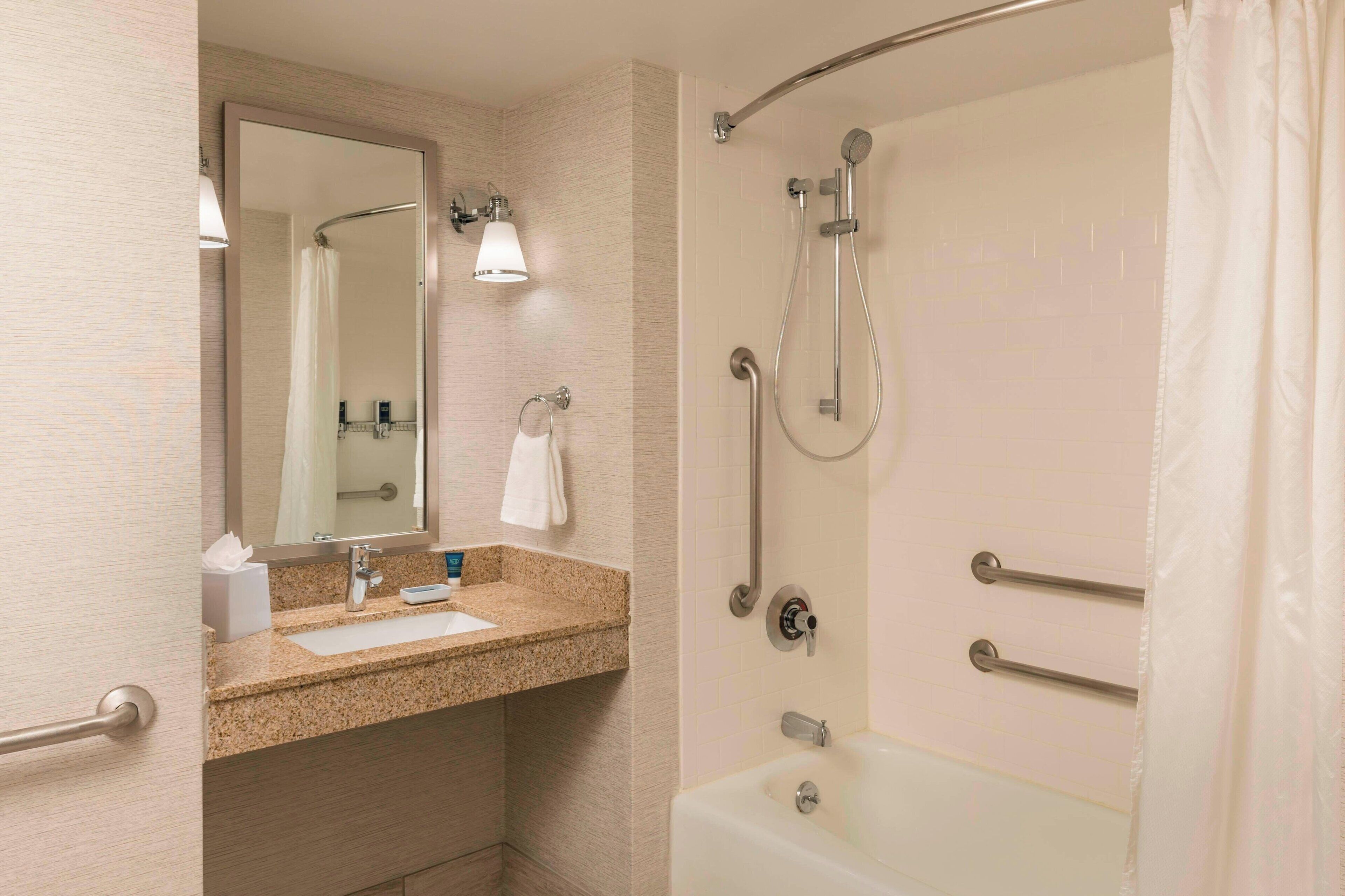 A bathroom with a sink, mirror, towel rack, and a walk-in shower with grab bars.