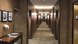 Un pasillo de hotel con paneles de madera, obras de arte enmarcadas en las paredes, un mostrador de recepción con un jarrón de flores y un piso alfombrado.