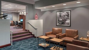 A lobby with a reception desk, a staircase, leather chairs, a coffee table, and a framed picture on the wall. - Four Points by Sheraton Boston Logan Airport Revere (Revere)