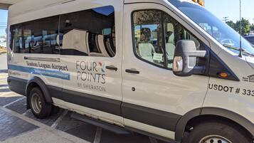 Una camioneta blanca con la marca "Four Points by Sheraton", estacionada en un aeropuerto.