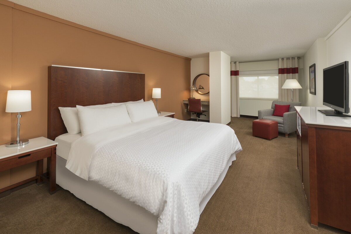 Habitación de hotel con una cama grande, un escritorio, una silla, un televisor y una ventana con cortinas.