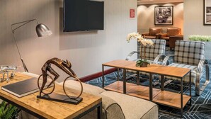 Un hall de hotel moderno con un televisor de pantalla plana, asientos cómodos, una mesa de centro de madera y una escultura metálica decorativa.
