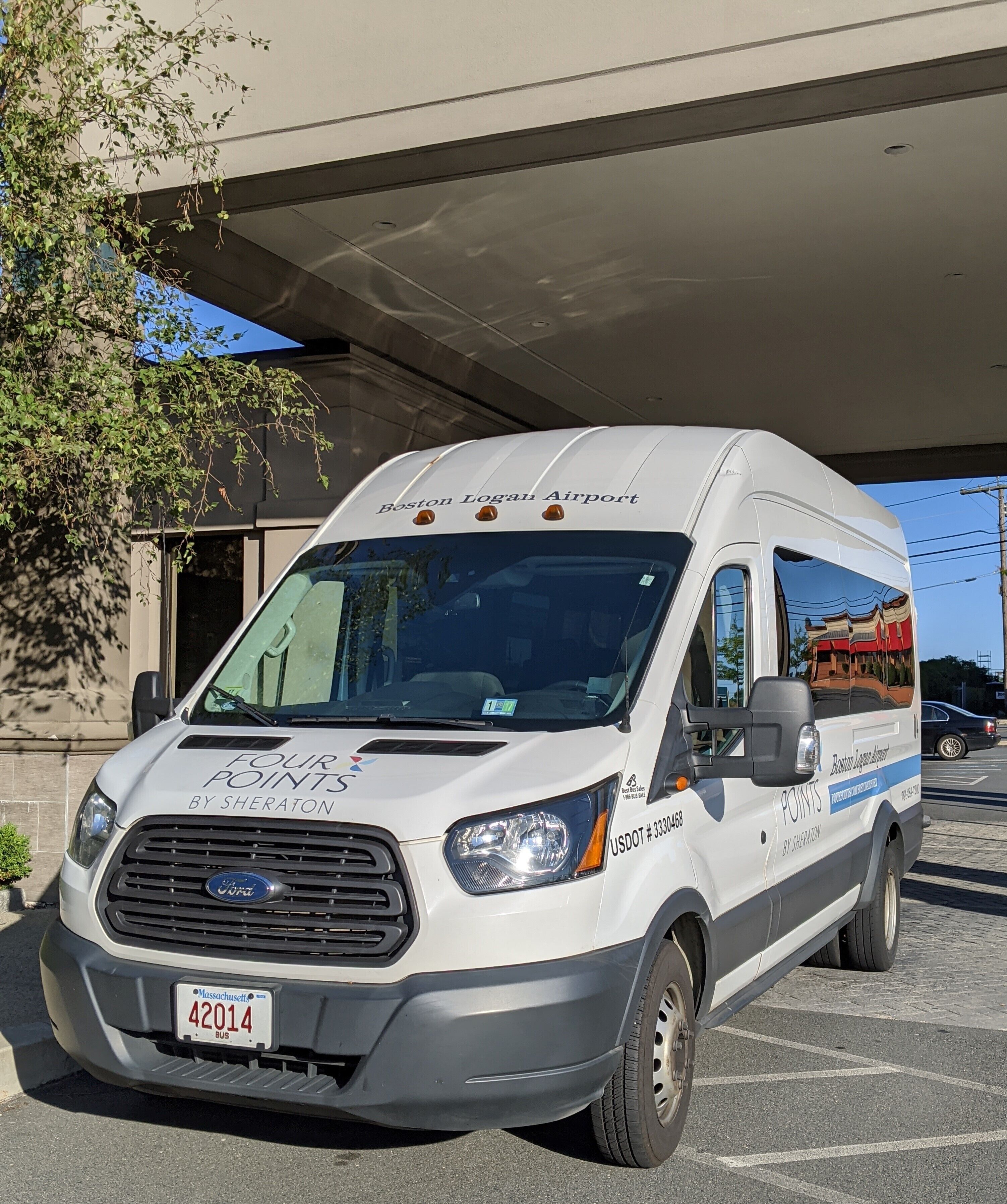 A white van with "Boston Logan Airport" and "FOUR POINTS BY SHERATON" written on it, parked under a bridge.