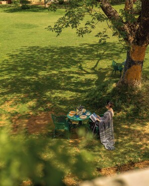 A dining table set outdoors with chairs, a person seated, and a tree nearby. - Resort Country Club, Manesar - WorldHotels Distinctive (Gurugram)