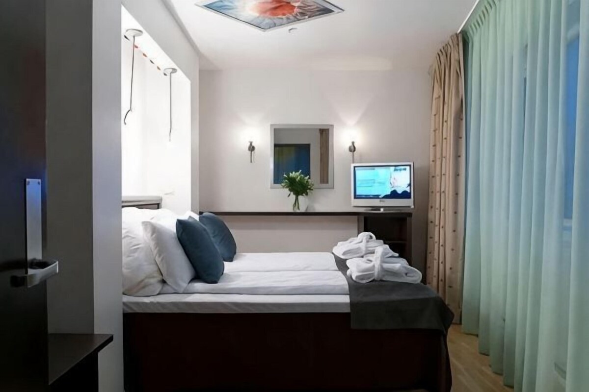 A hotel room with a bed, a desk with a computer, a TV, and a window with curtains.
