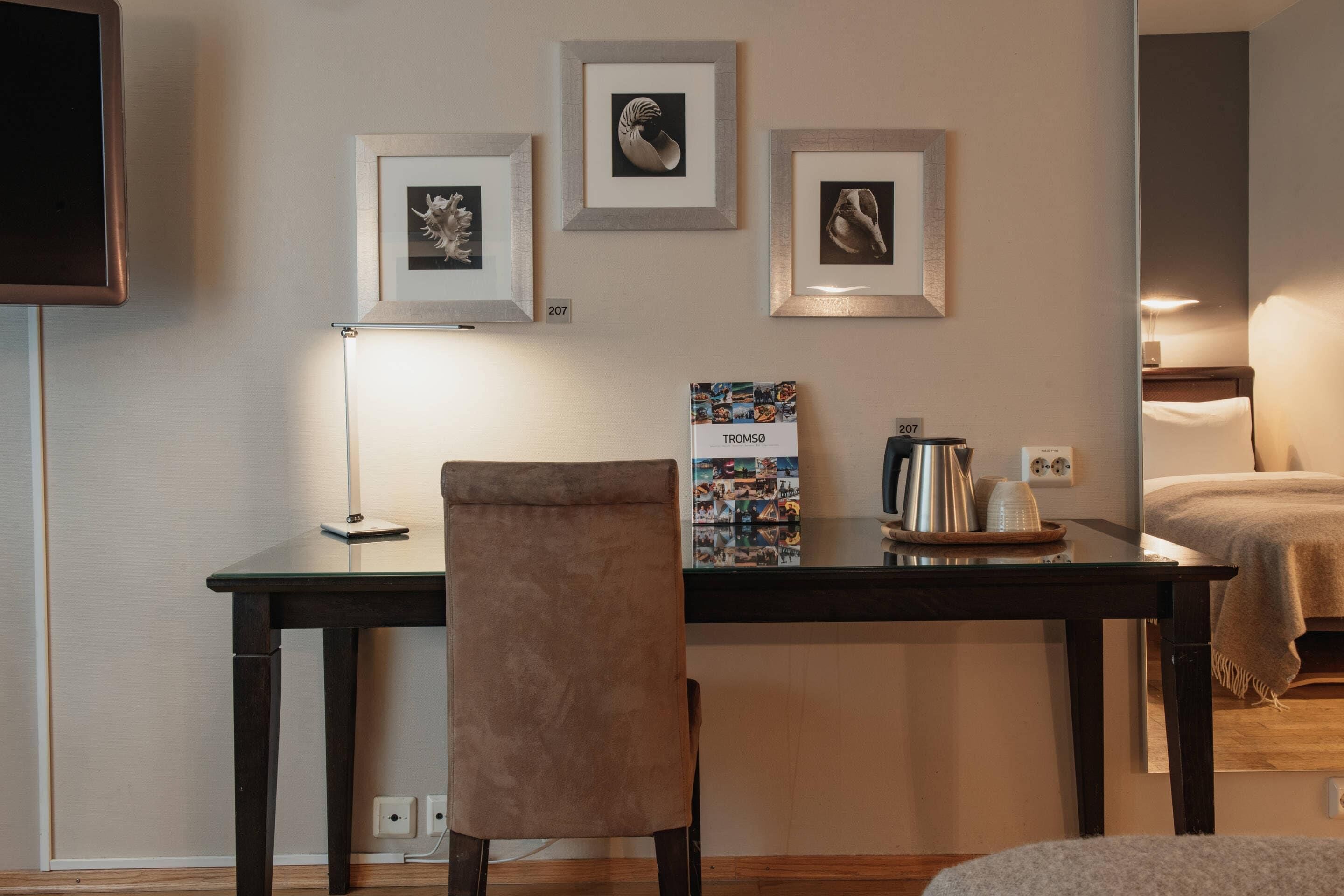 Une chambre d’hôtel avec un lit, un bureau et une chaise, une télévision et des tableaux encadrés au mur.