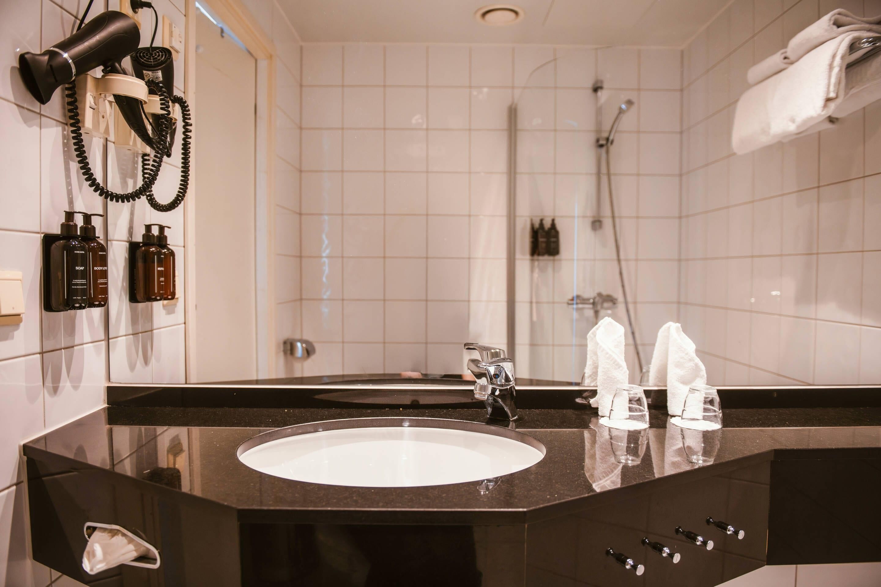 Een badkamer met een zwart wastafel, een spiegel, een haardroger en een douche.