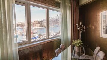 Una habitación con un ventanal grande con vistas a un puerto deportivo, una mesa de comedor con sillas y una planta en maceta.