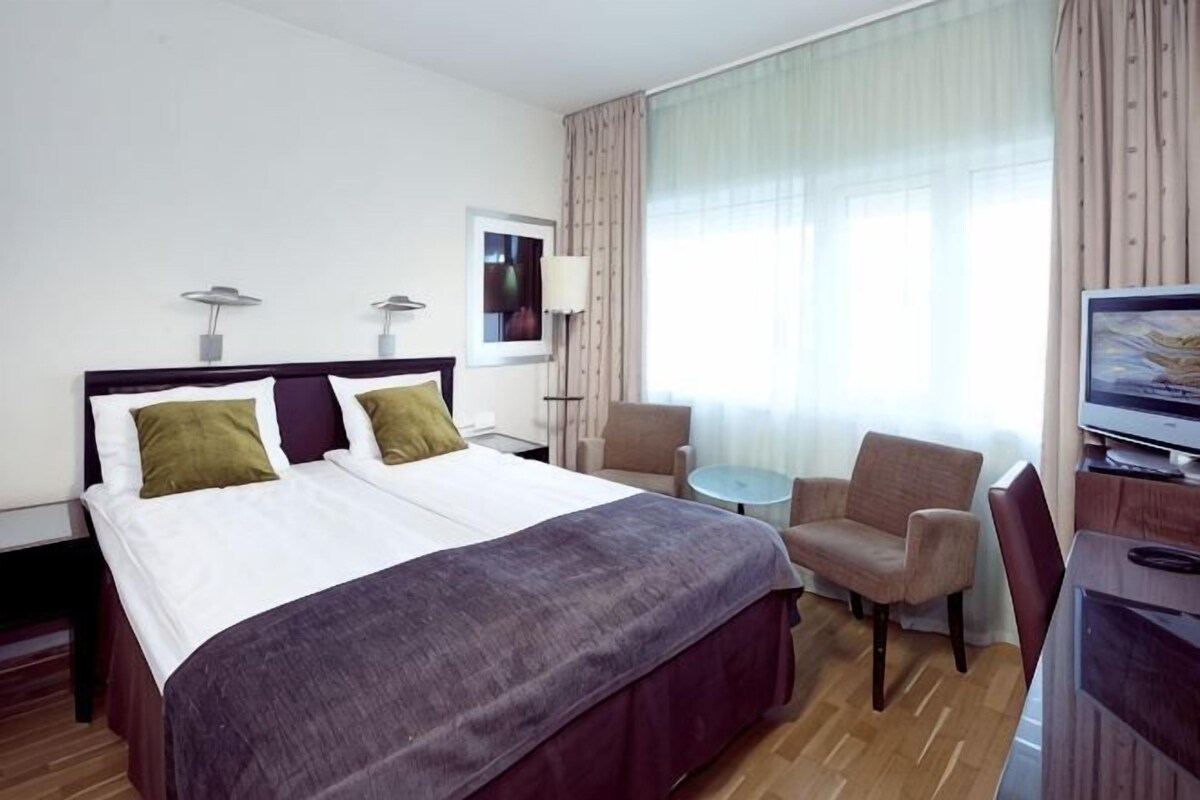 A hotel room with a bed, a chair, a desk, and a television.