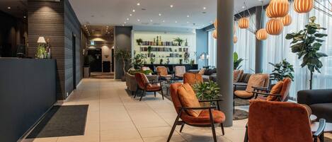 A modern lobby with a reception desk, seating area, and a bookshelf filled with books.
