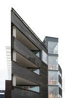 Un hotel moderno con fachada oscura, varios balcones y ventanas grandes.