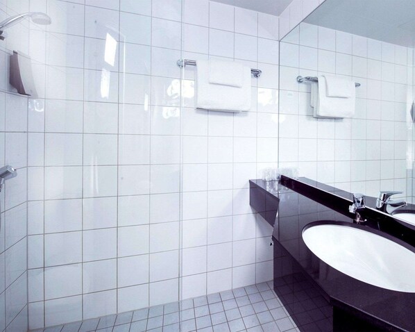 A modern bathroom with white tiles, a black sink, and a glass shower enclosure.