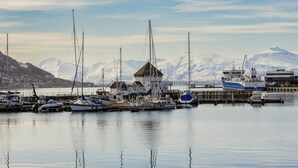 A marina with boats docked, a building with a pointed roof, and snow-capped mountains in the background. - Home Hotel Aurora (Tromsø)