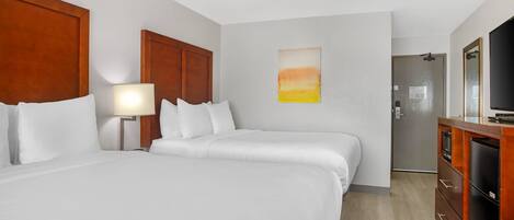 Habitación de hotel con dos camas, un escritorio, un televisor y la puerta del baño.