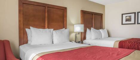 A hotel room with two beds, a red armchair, and a lamp.