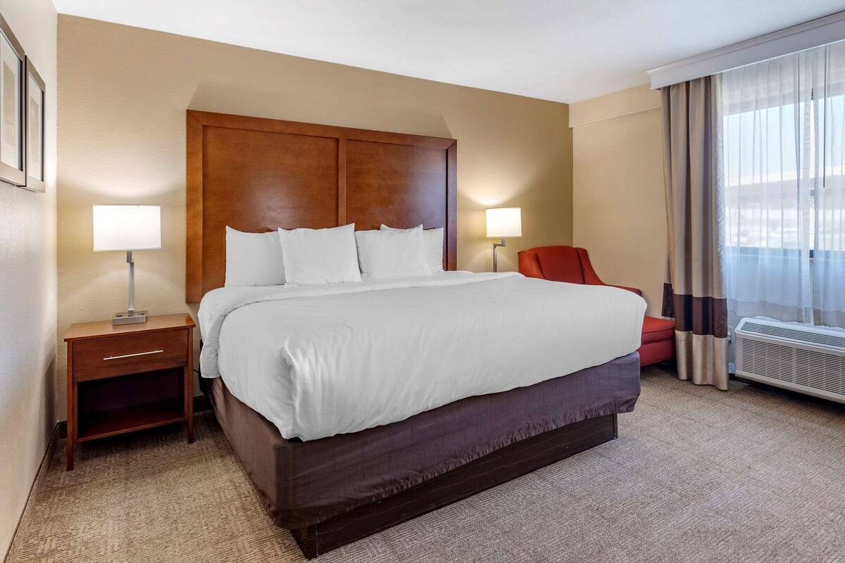 A hotel room with a large bed, two bedside tables, a red chair, and a window with curtains.