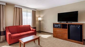 Habitación de hotel con sofá rojo, una mesa de centro de madera, televisor de pantalla plana, microondas y refrigerador pequeño.