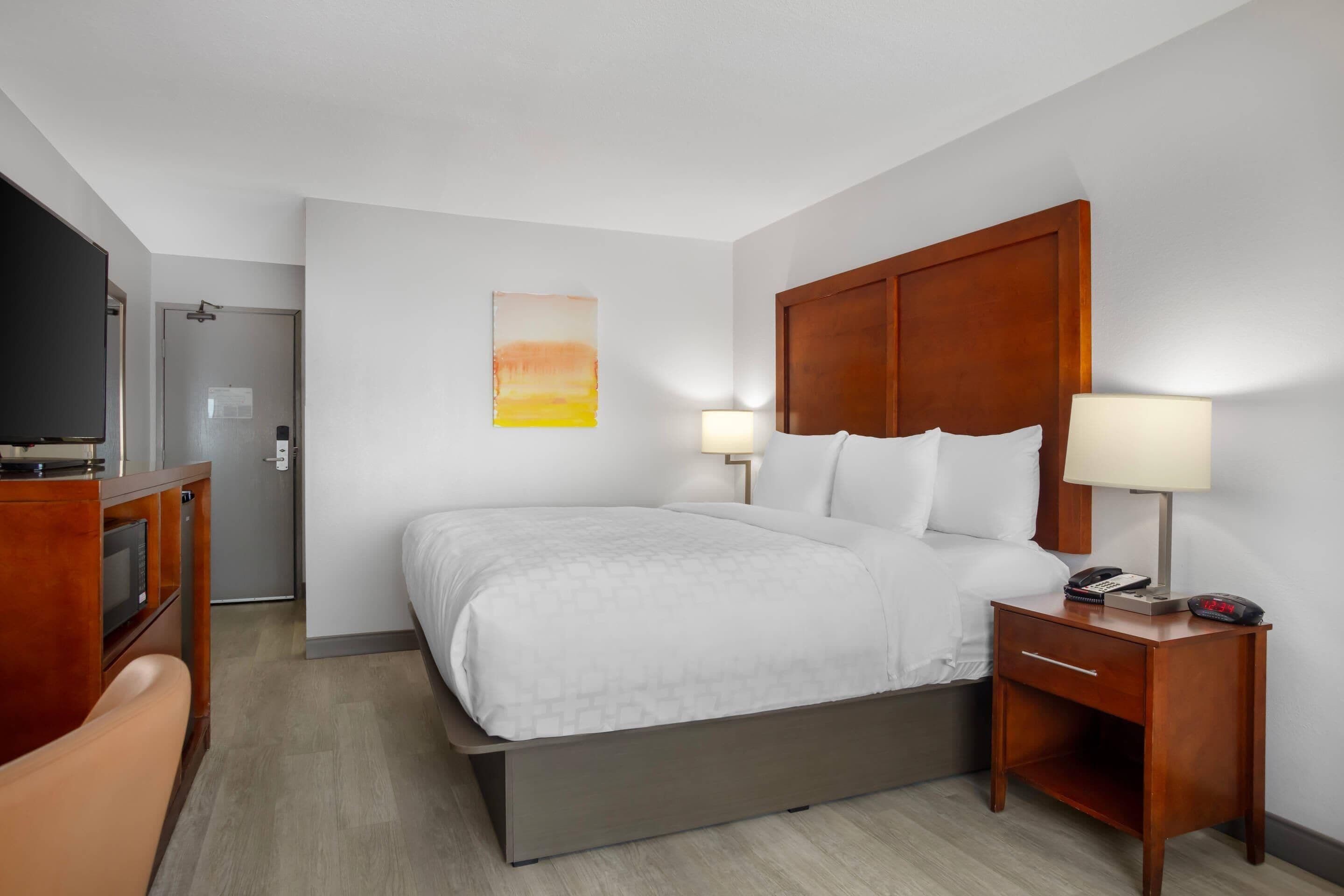 Una habitación de hotel con cama, mesita de noche, lámpara y televisor.