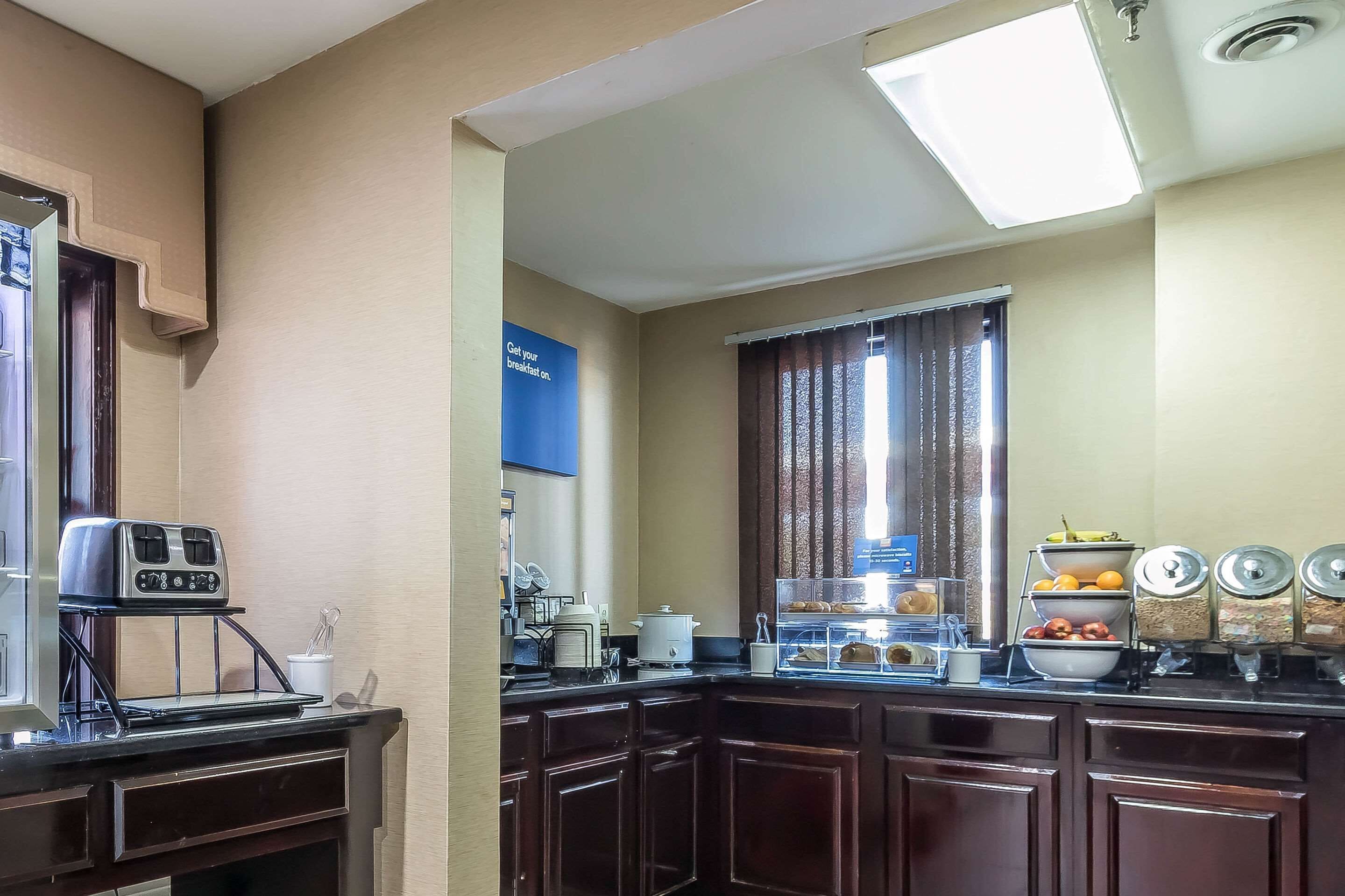 Cocina equipada con tostadora, cafetera y barra desayunadora. Se observan armarios y una ventana con cortinas.
