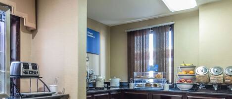 Cocina equipada con tostadora, cafetera y barra desayunadora. Se observan armarios y una ventana con cortinas.