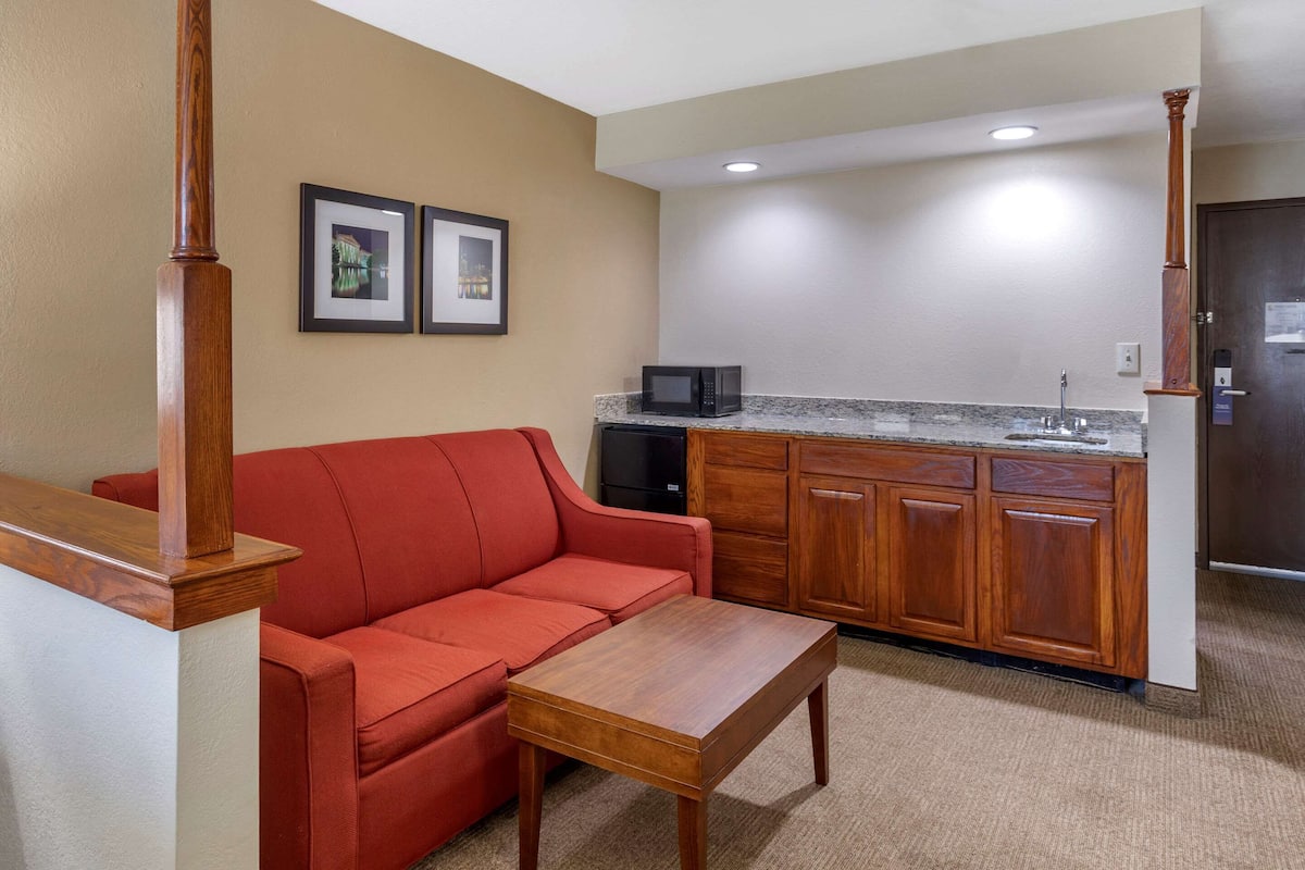 A compact living space with a red sofa, a wooden coffee table, a kitchen area with a microwave, and wooden cabinets.