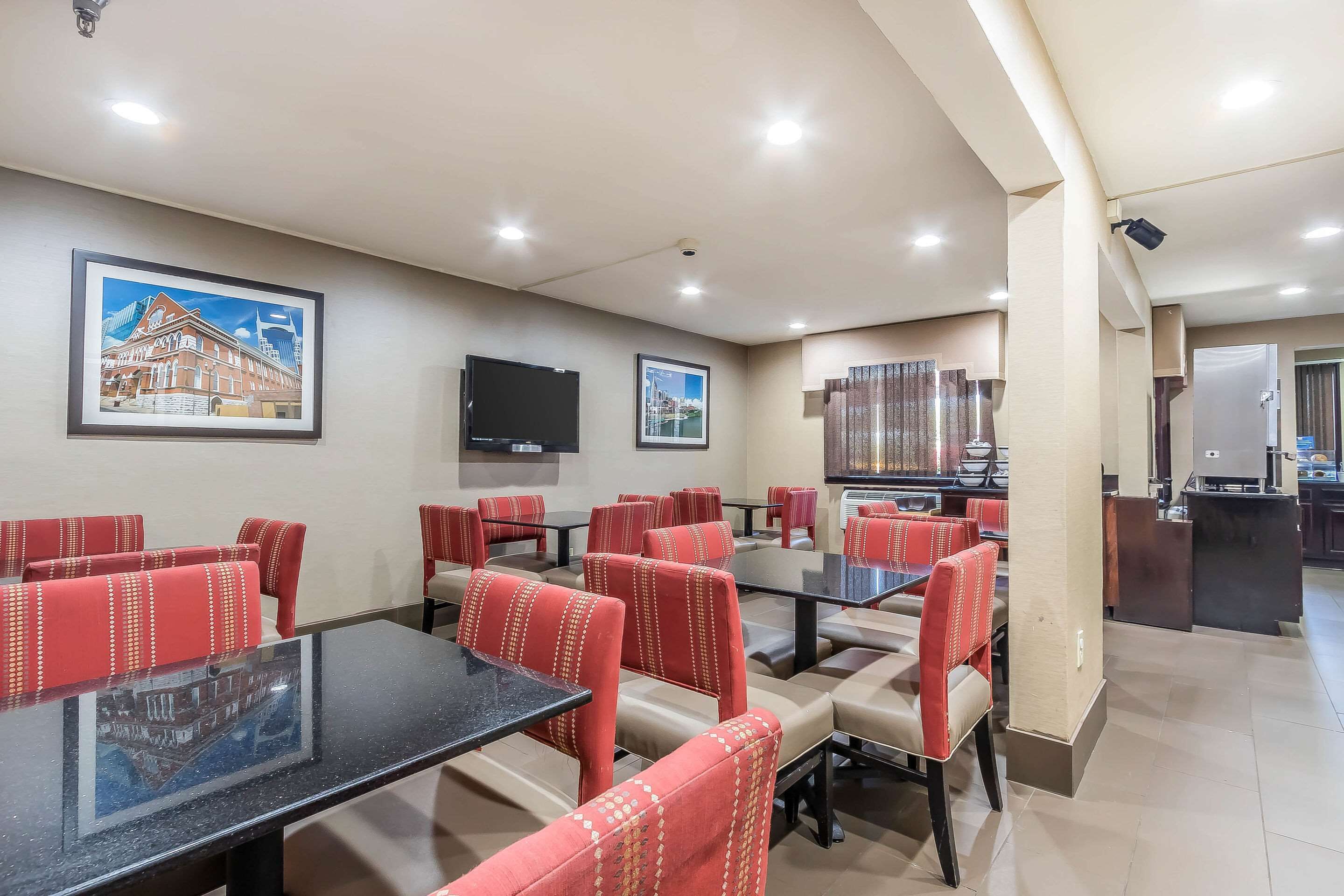 A restaurant with red upholstered booths, black tables, and a flat-screen TV on the wall.