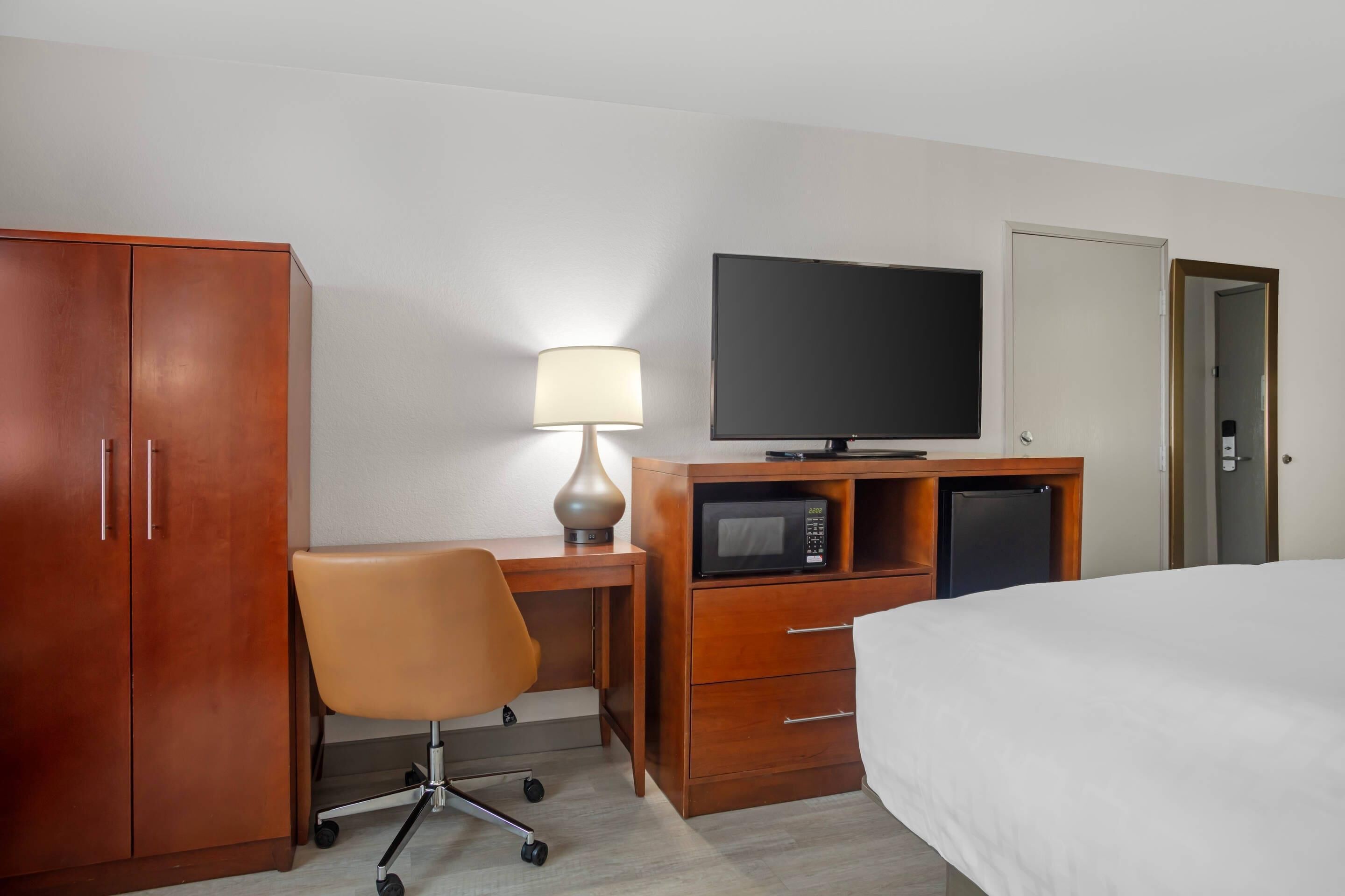 Une chambre d’hôtel comprenant un lit, un bureau avec une lampe, une télévision, un four à micro-ondes et une armoire.