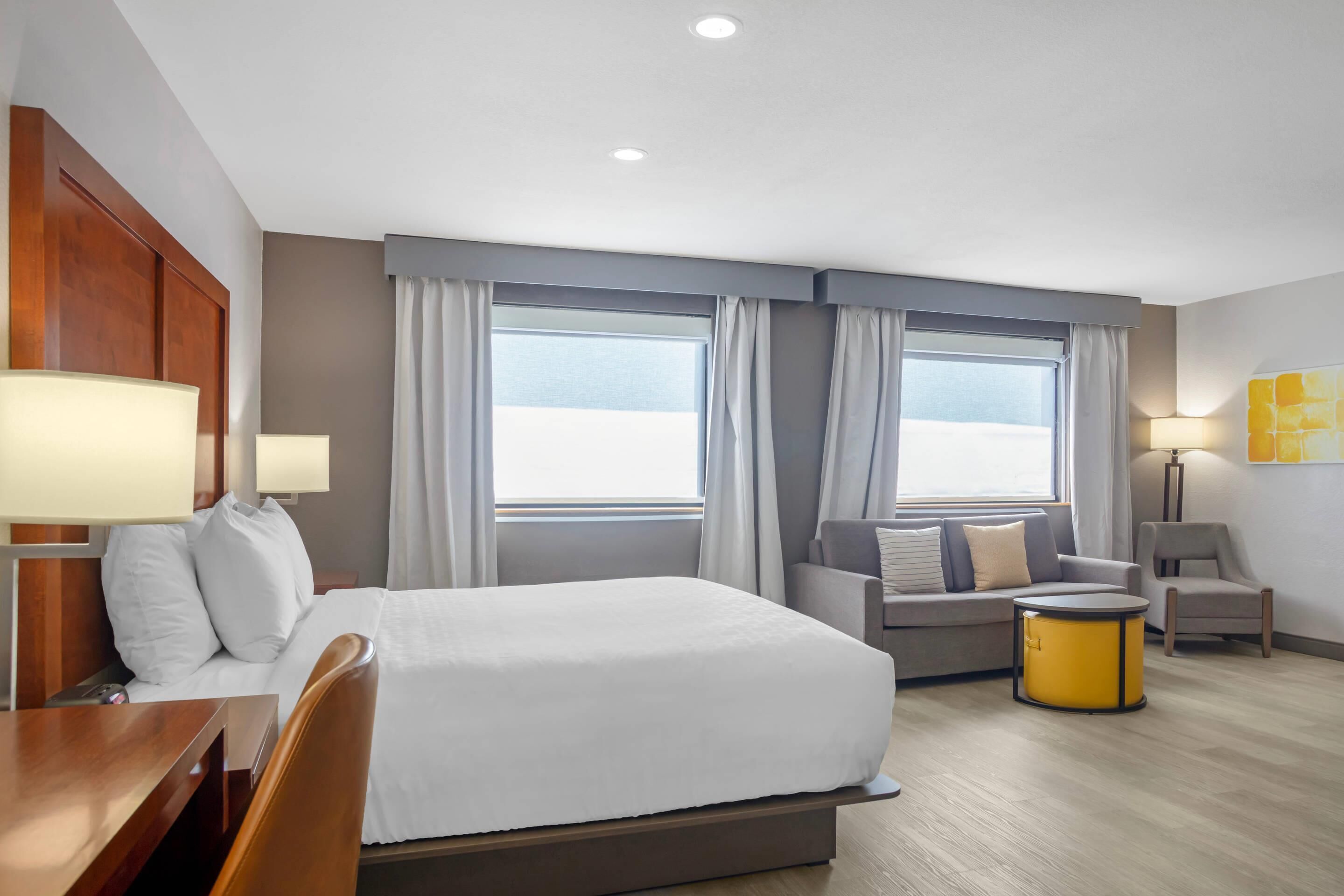 A hotel room with a bed, a sofa, a small table, a chair, and a lamp.
