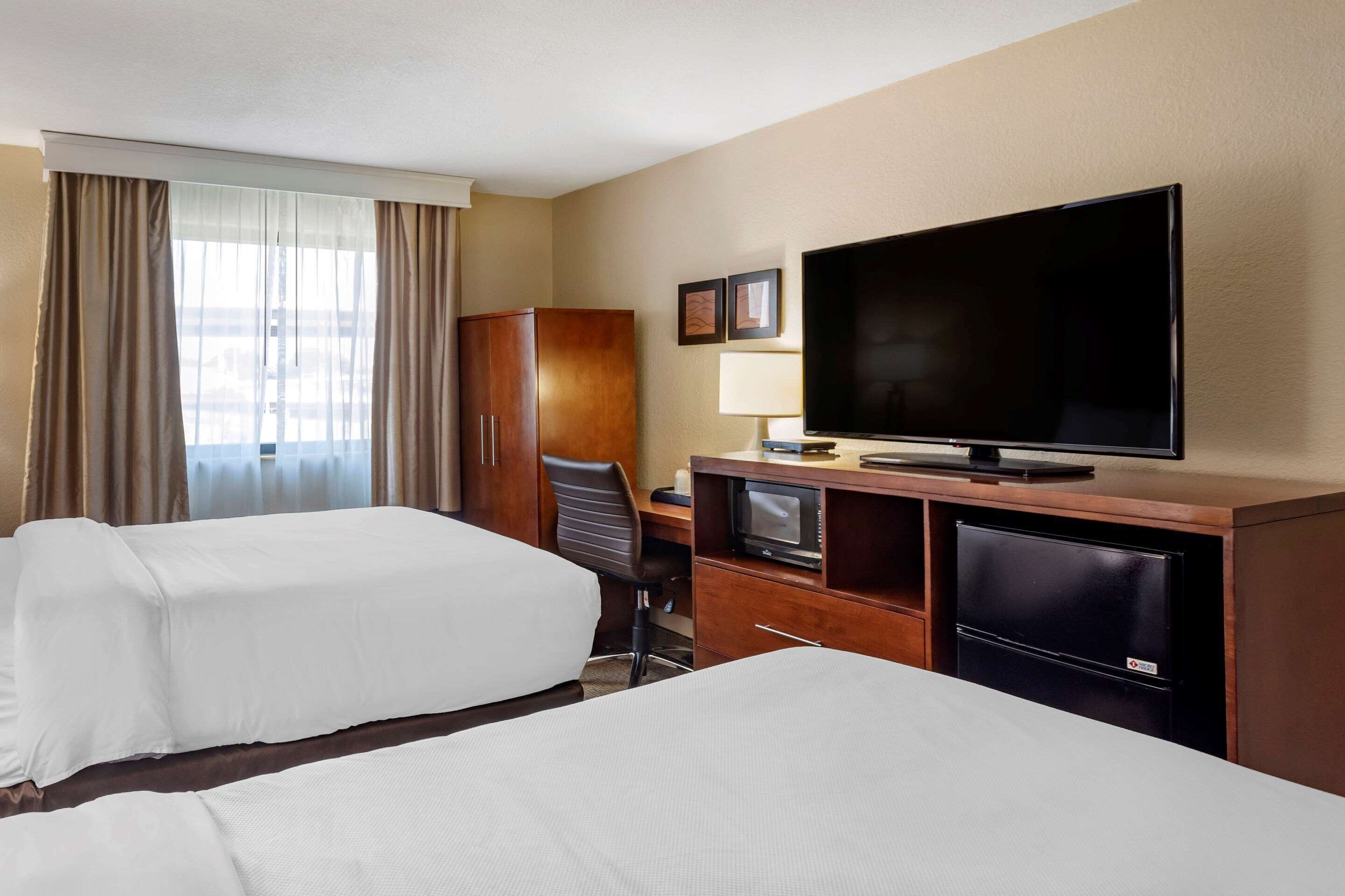 A hotel room with two beds, a desk with a television, a microwave, and a wardrobe.
