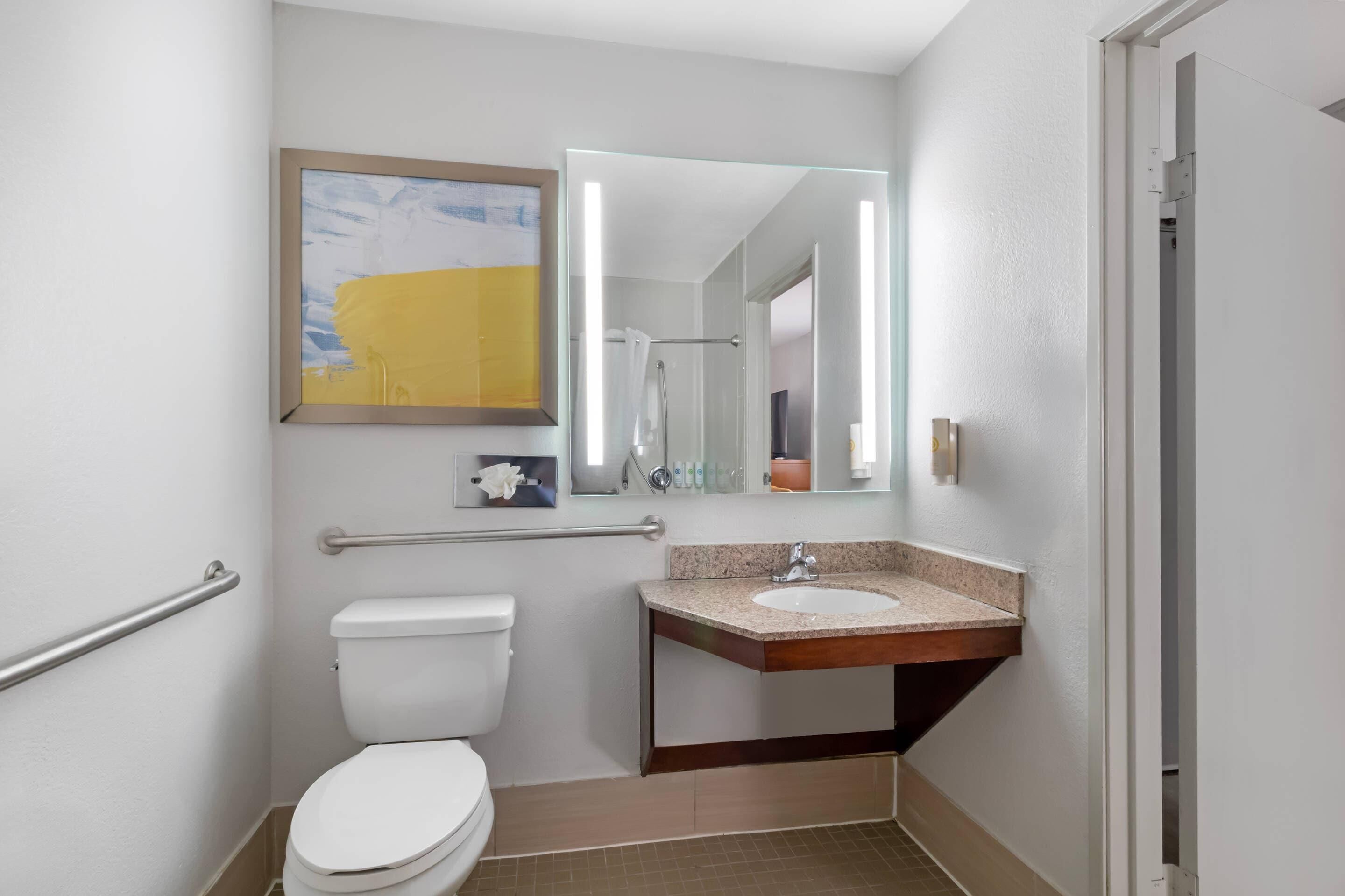 Un baño de hotel estándar con inodoro, lavamanos y barandal.